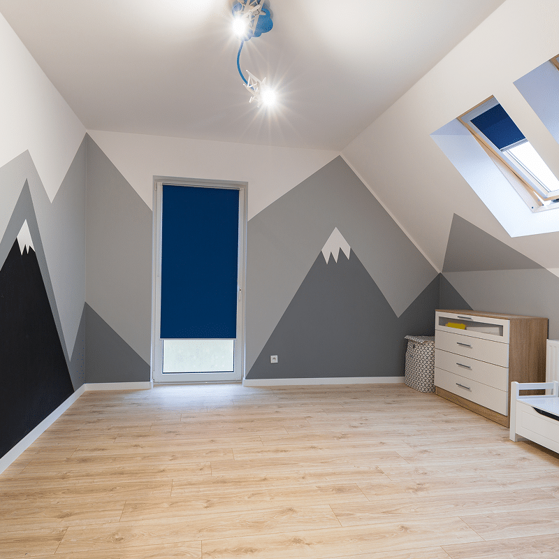Chambre d'enfant moderne avec murale montagnes grises, sol bois clair. Volets bleus aux fenêtres et puits de lumière. Commode en bois.