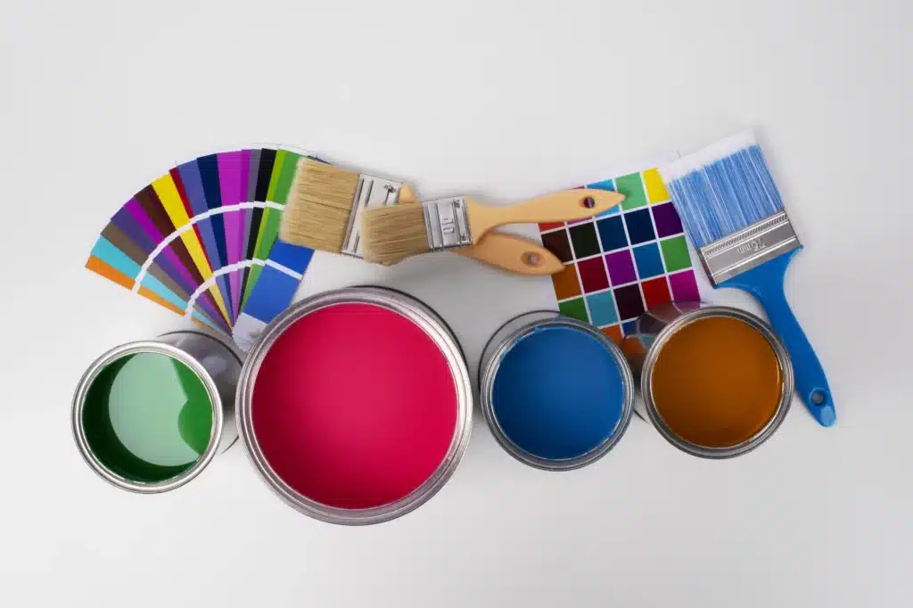 Pots de peinture ouverts (vert, rouge, bleu, orange), 3 pinceaux (un de 75 mm) et 2 nuanciers de couleurs sur fond blanc.